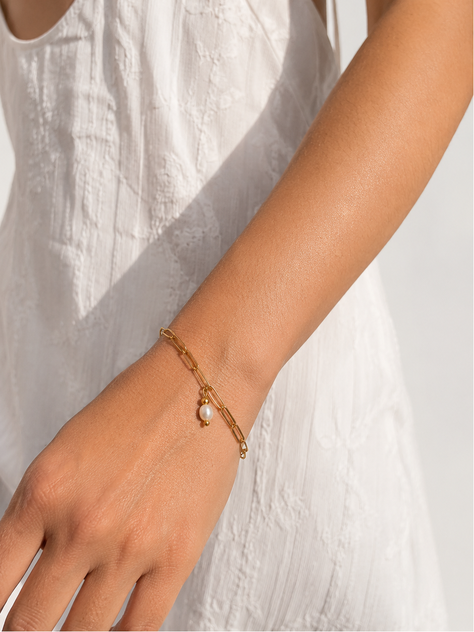 Woman in a white dress wearing a gold paperclip-chain bracelet with an oval white pearl pendant