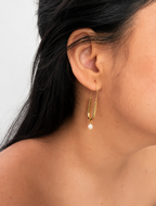 Close-up of a gold paperclip drop earring with an oval white freshwater pearl worn on the ear