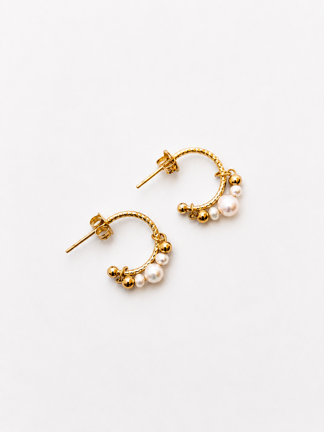 Lifestyle view of small gold creole earrings with white freshwater pearl clusters worn on the ear