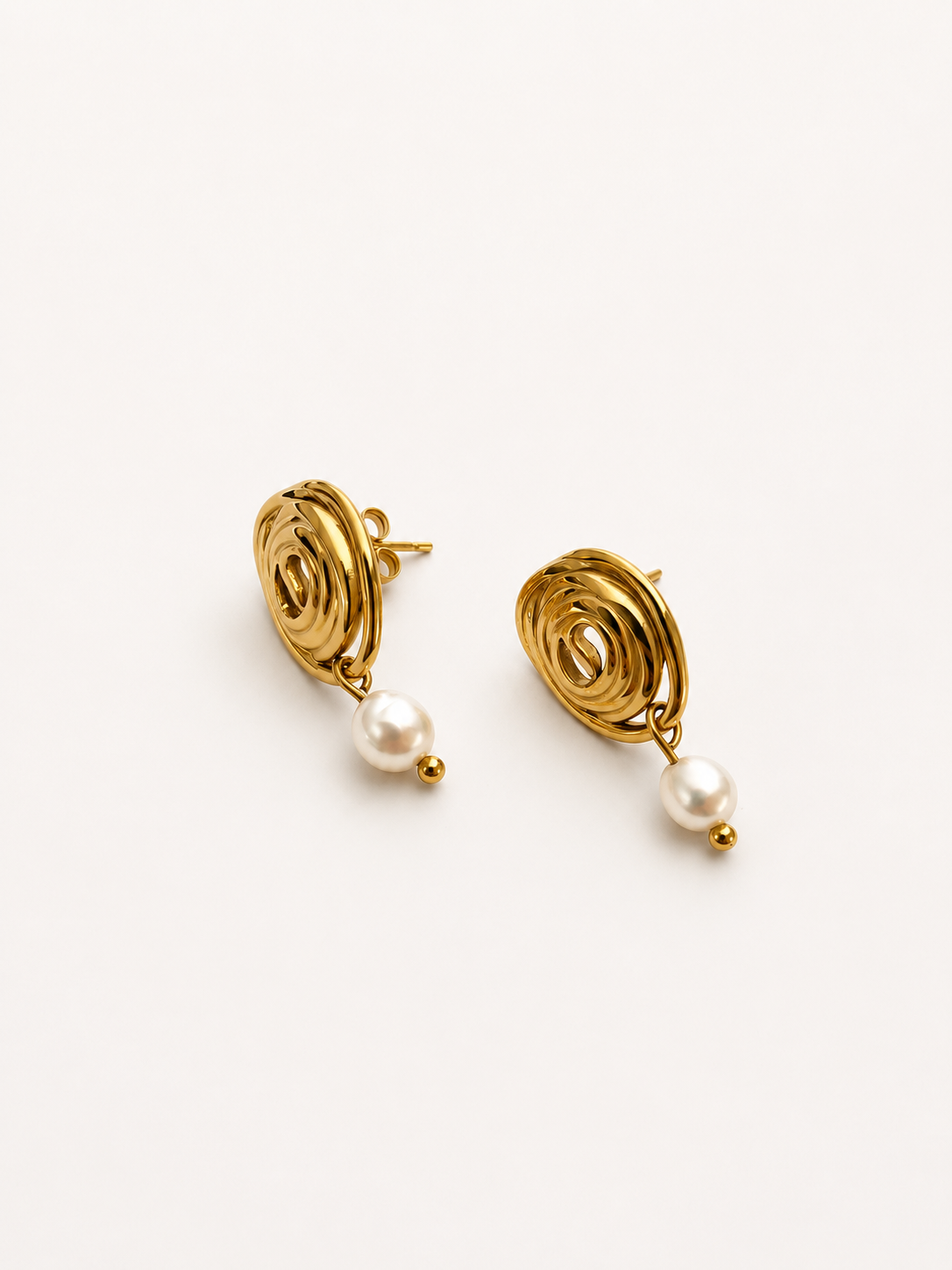 Angled pair of sculptural gold spiral stud earrings with oval white freshwater pearl drops
