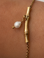 Close-up of an oval white freshwater pearl suspended from a sculpted gold twig bracelet