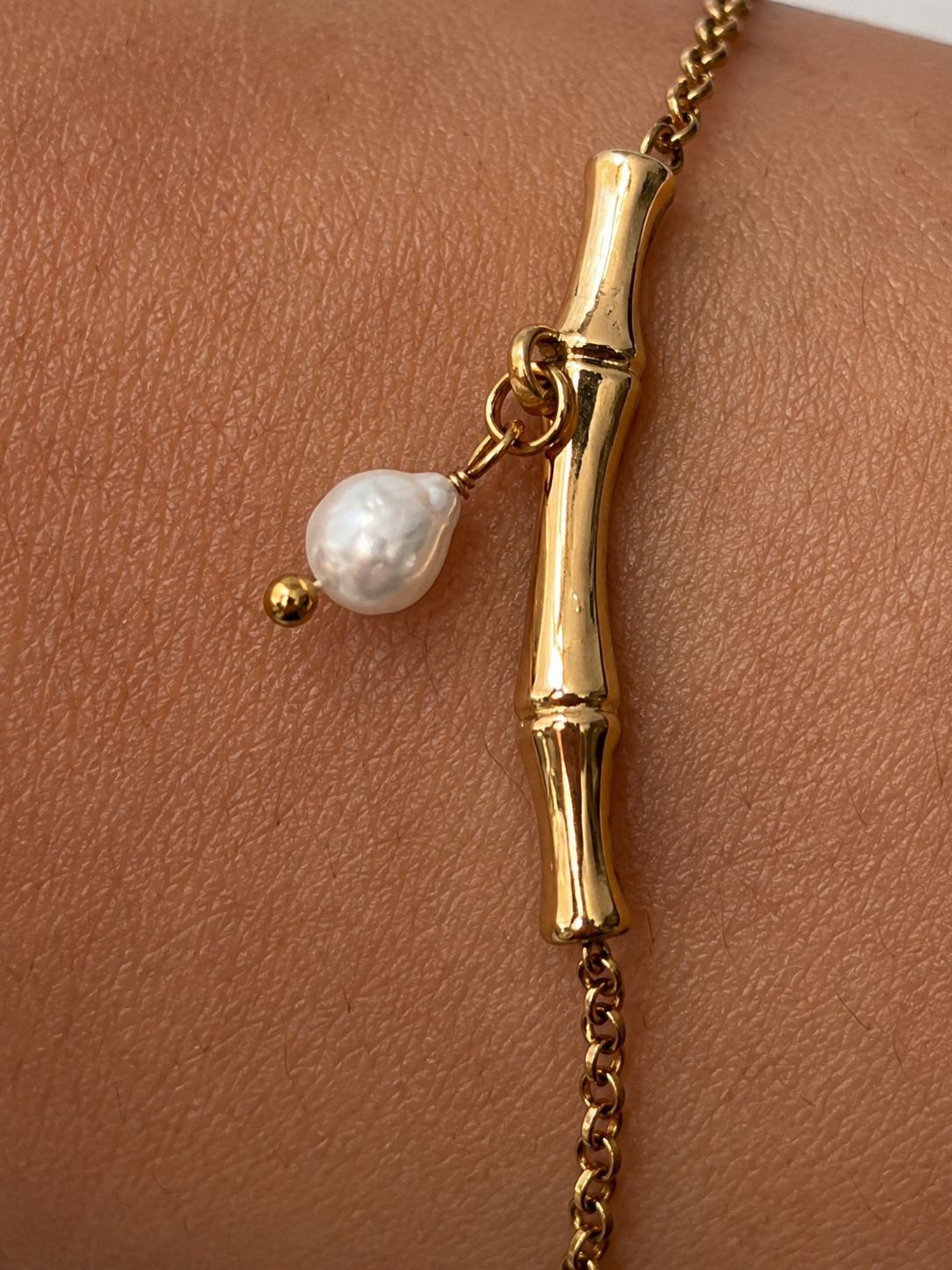 Close-up of an oval white freshwater pearl suspended from a sculpted gold twig bracelet