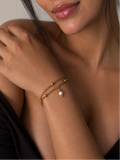 Woman wearing a twisted gold double-chain bracelet with a white freshwater pearl drop and polished beads