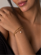 Woman wearing a twisted gold double-chain bracelet with a white freshwater pearl drop and polished beads