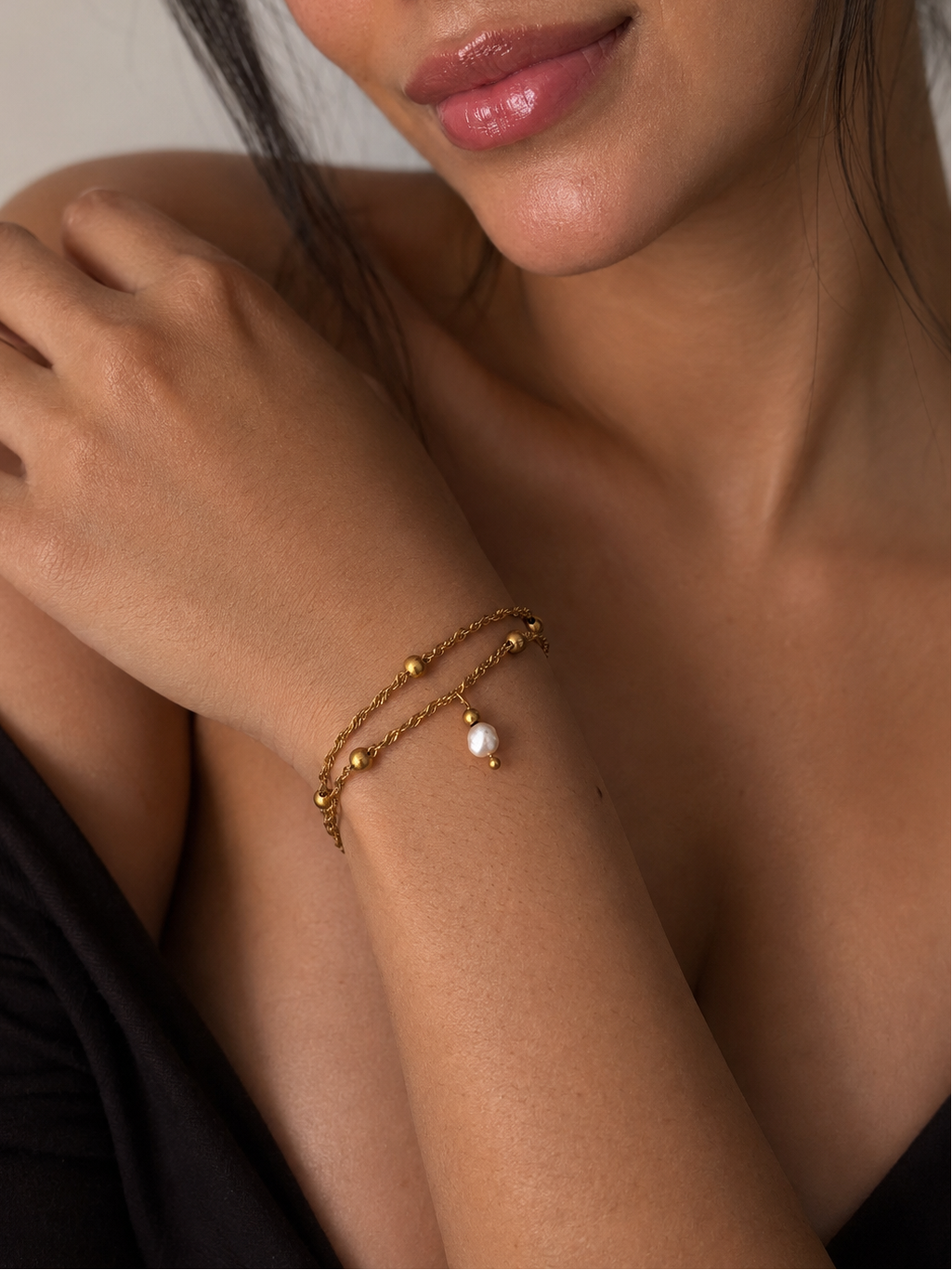 Woman wearing a twisted gold double-chain bracelet with a white freshwater pearl drop and polished beads