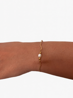 Close-up of a gold wave-chain bracelet with an oval white freshwater pearl on the wris