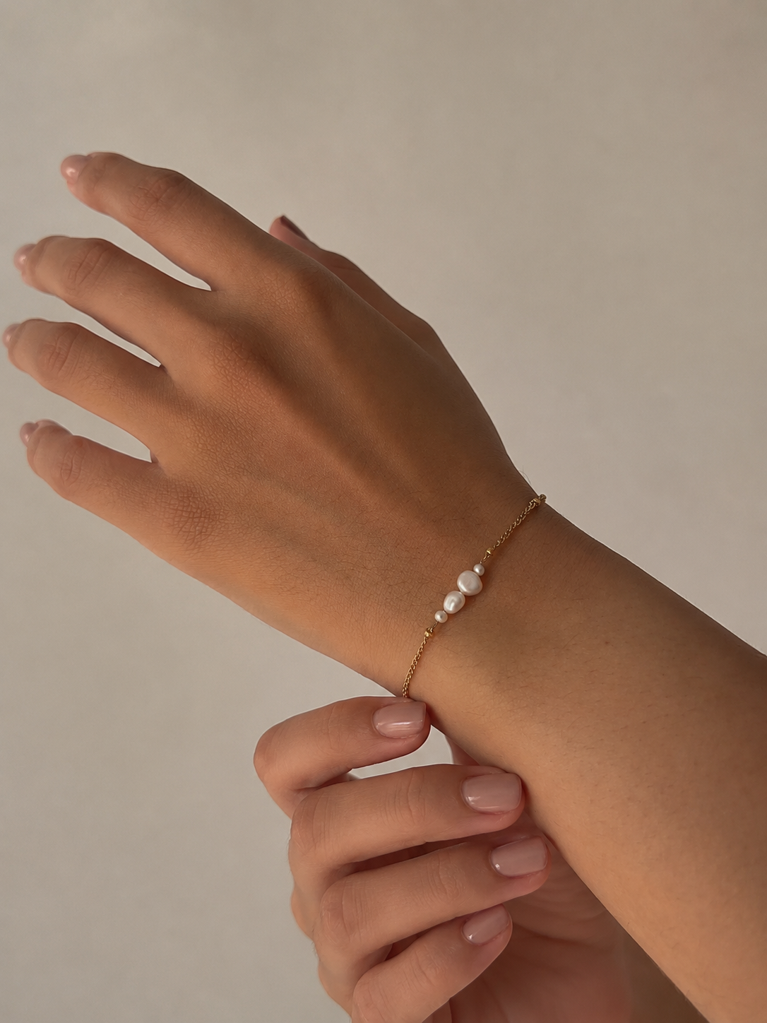 Close-up of a delicate gold bracelet with mixed-size white baroque freshwater pearls on the wrist